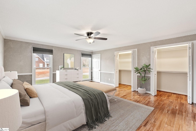 bedroom featuring ornamental molding, multiple windows, wood finished floors, and two closets