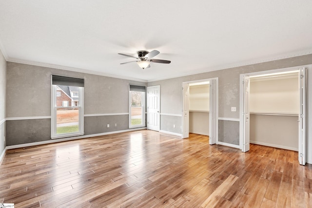 unfurnished bedroom featuring baseboards, wood finished floors, two closets, and crown molding