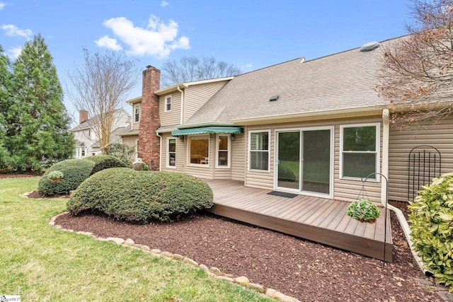 back of property with a chimney, a deck, a lawn, and roof with shingles