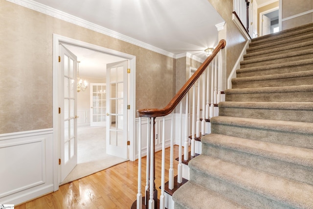 staircase featuring french doors, a wainscoted wall, a decorative wall, ornamental molding, and wood finished floors