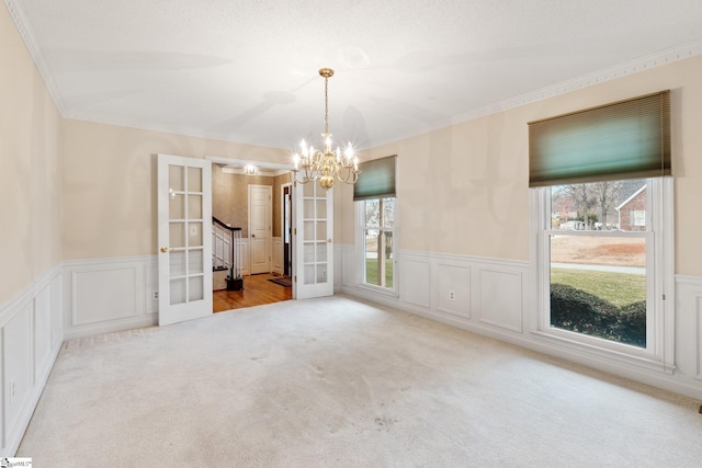 carpeted empty room featuring crown molding, french doors, a wainscoted wall, and a healthy amount of sunlight