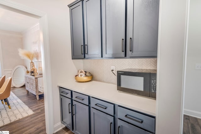 kitchen with black microwave, gray cabinets, tasteful backsplash, dark wood finished floors, and crown molding