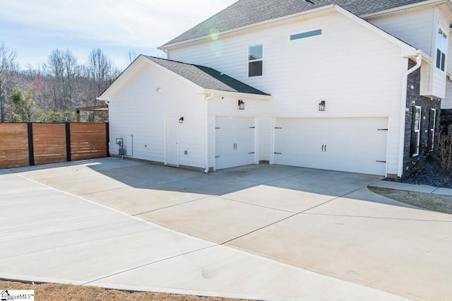 view of home's exterior with a garage, driveway, fence, and a shingled roof