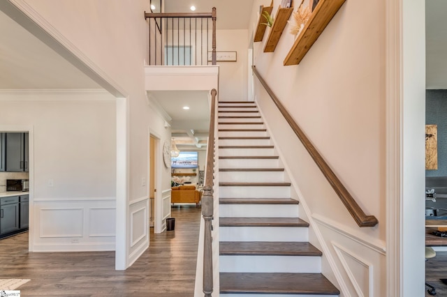 stairs featuring a wainscoted wall, crown molding, a decorative wall, a high ceiling, and wood finished floors