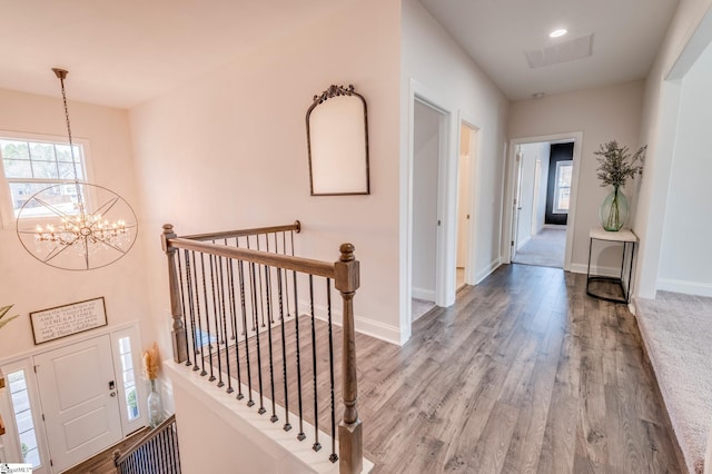 hallway featuring an inviting chandelier, baseboards, wood finished floors, and an upstairs landing