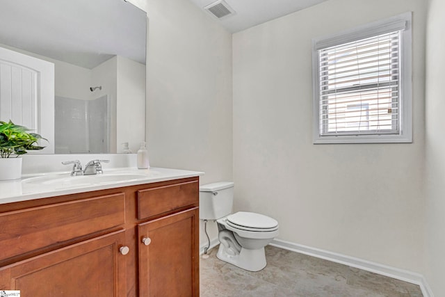 bathroom featuring toilet, vanity, visible vents, baseboards, and walk in shower