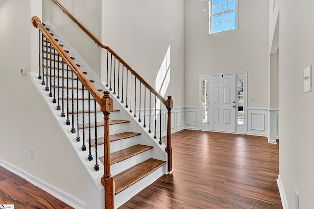 entrance foyer featuring a wainscoted wall, dark wood-type flooring, stairs, a high ceiling, and a decorative wall