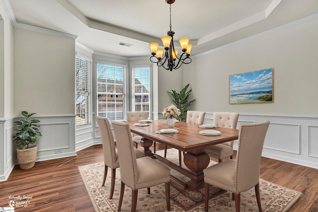 dining area with dark wood-style floors, a tray ceiling, a notable chandelier, a decorative wall, and ornamental molding