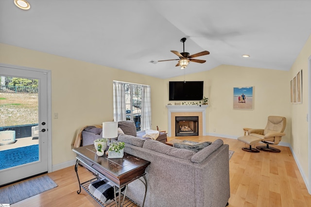 living area with lofted ceiling, light wood-style flooring, a tiled fireplace, and a wealth of natural light