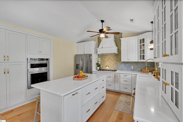 kitchen with visible vents, appliances with stainless steel finishes, vaulted ceiling, a sink, and premium range hood