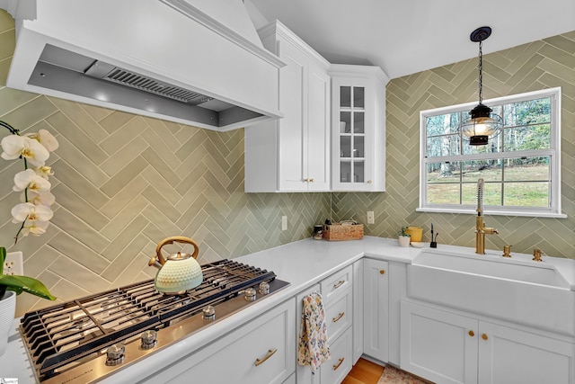 kitchen with tasteful backsplash, white cabinets, custom range hood, stainless steel gas stovetop, and a sink