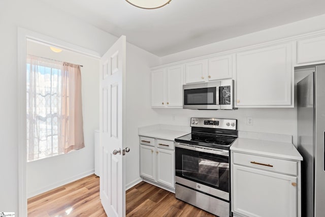 kitchen with appliances with stainless steel finishes, light countertops, white cabinetry, and wood finished floors