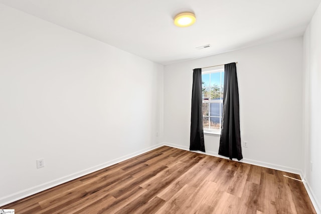 unfurnished room featuring visible vents, baseboards, and wood finished floors