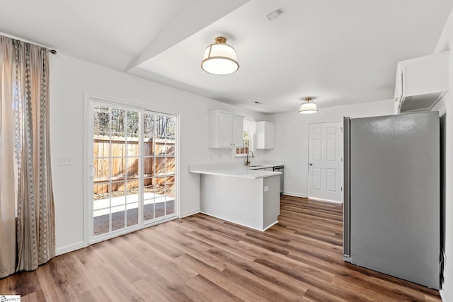 kitchen featuring white cabinets, wood finished floors, freestanding refrigerator, a peninsula, and light countertops