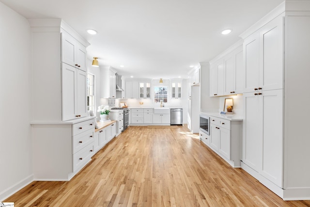 kitchen with appliances with stainless steel finishes, light wood-type flooring, a sink, and white cabinets