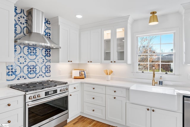 kitchen with a sink, white cabinetry, light countertops, wall chimney range hood, and appliances with stainless steel finishes