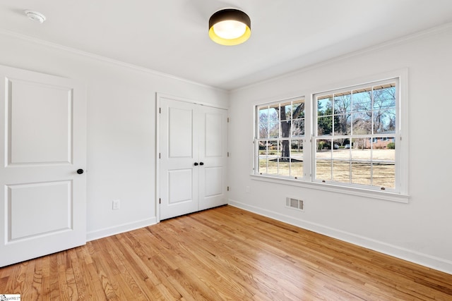 unfurnished bedroom featuring visible vents, baseboards, a closet, light wood-type flooring, and crown molding