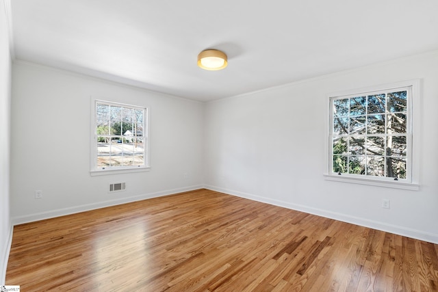 spare room featuring light wood-style flooring, visible vents, baseboards, and ornamental molding