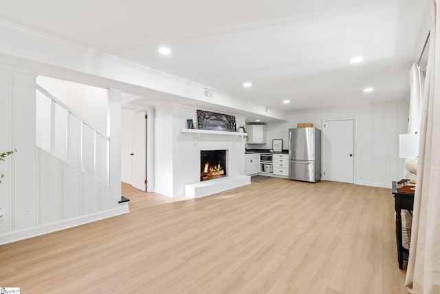 unfurnished living room featuring stairway, ornamental molding, a lit fireplace, light wood-style floors, and recessed lighting