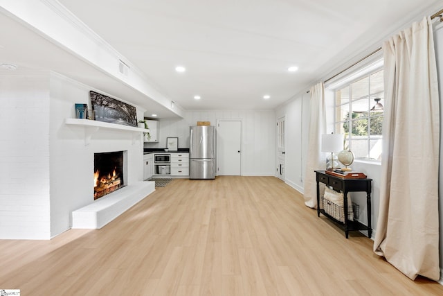 living room with crown molding, a brick fireplace, visible vents, and light wood-style floors