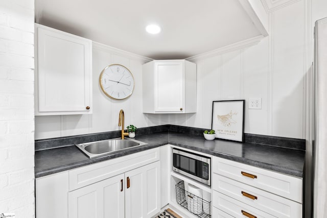 kitchen featuring dark countertops, stainless steel microwave, white cabinets, and a sink