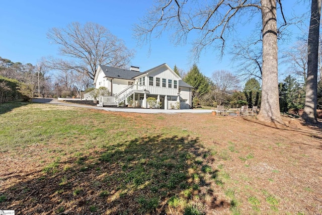 rear view of property with board and batten siding, a chimney, a lawn, and stairway