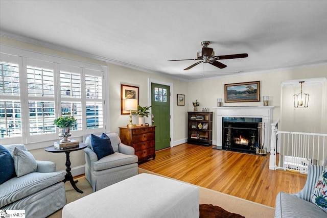 living area featuring light wood finished floors, baseboards, a ceiling fan, ornamental molding, and a fireplace