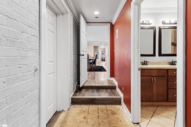 hall with crown molding, light tile patterned flooring, a sink, brick wall, and baseboards