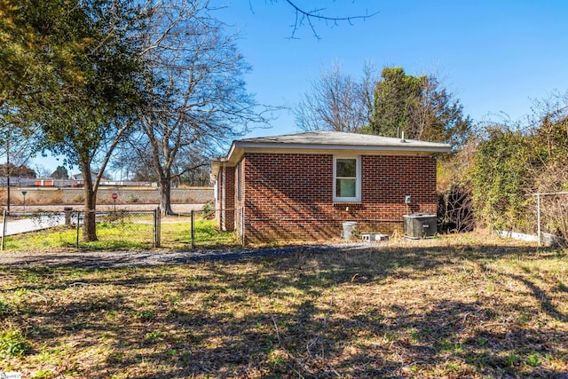 view of home's exterior with a gate, brick siding, fence, and central air condition unit