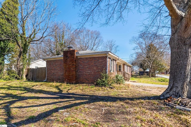 view of property exterior with a yard, a chimney, fence, and brick siding