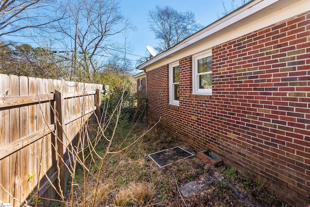 view of side of property featuring crawl space, brick siding, and fence