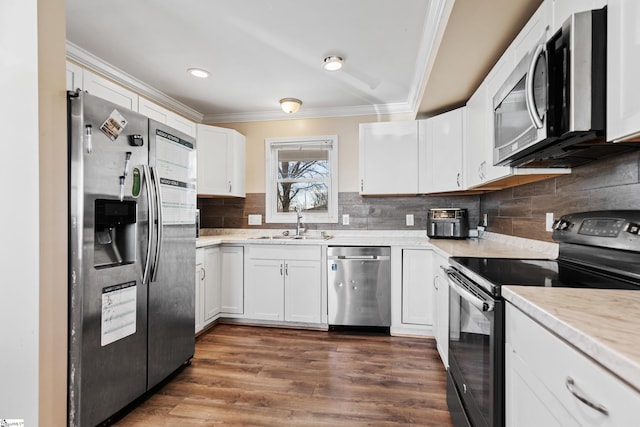 kitchen with appliances with stainless steel finishes, dark wood-type flooring, ornamental molding, white cabinetry, and a sink