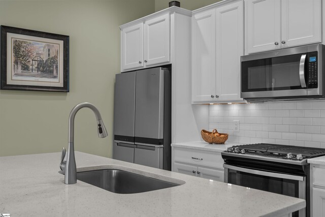 kitchen featuring stainless steel appliances, a sink, white cabinetry, decorative backsplash, and light stone countertops