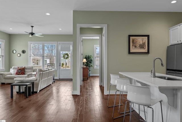 kitchen featuring a kitchen breakfast bar, dark wood-type flooring, white cabinetry, a sink, and recessed lighting