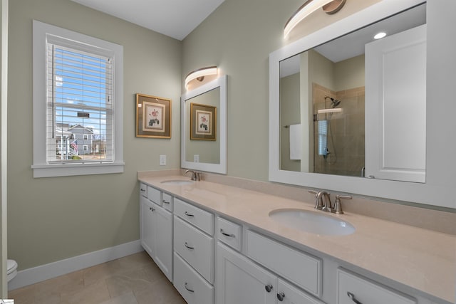 full bath with tiled shower, a sink, baseboards, and double vanity