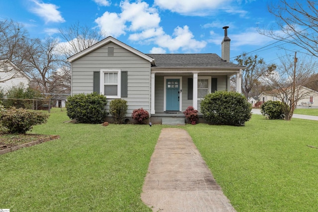 bungalow-style house featuring covered porch, roof with shingles, a chimney, and a front yard