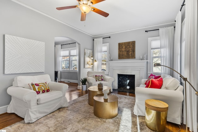 sitting room with arched walkways, wood finished floors, a wealth of natural light, and crown molding