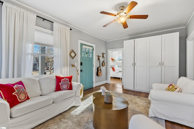 living room featuring a ceiling fan, baseboards, ornamental molding, and wood finished floors