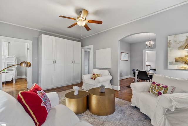 living room with arched walkways, crown molding, wood finished floors, baseboards, and ceiling fan with notable chandelier