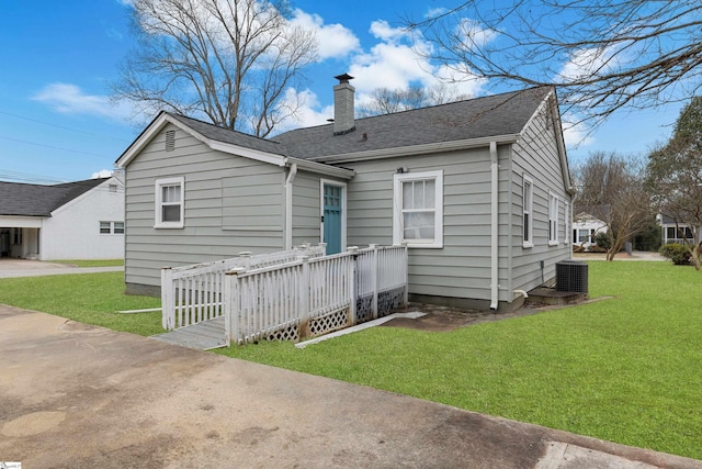 back of house with roof with shingles, a chimney, central AC, and a yard