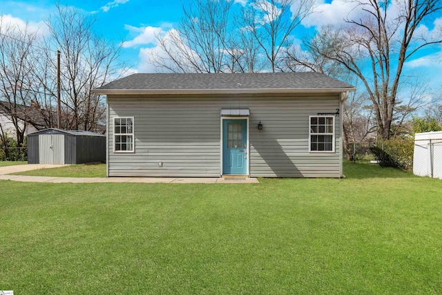 view of front facade with an outdoor structure, roof with shingles, fence, and a front lawn