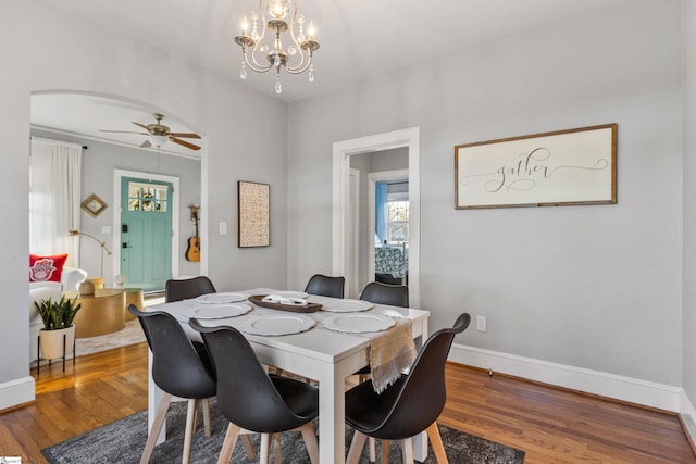 dining area with baseboards, arched walkways, wood finished floors, and ceiling fan with notable chandelier