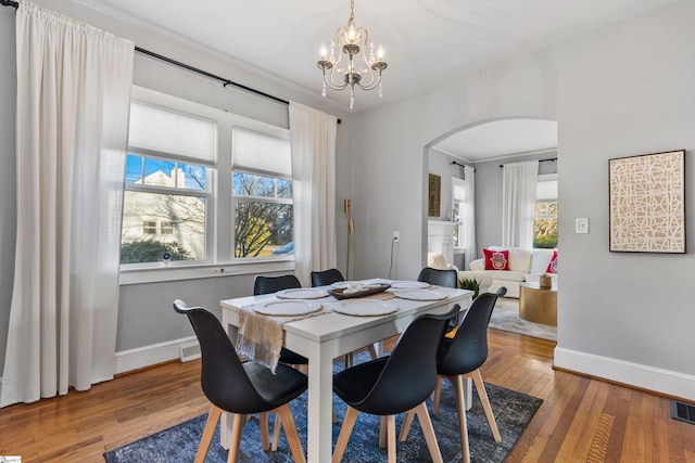 dining room featuring arched walkways, an inviting chandelier, hardwood / wood-style flooring, and baseboards