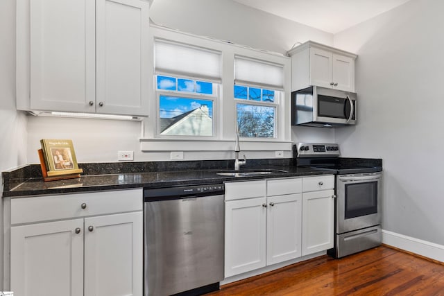 kitchen with baseboards, white cabinets, dark stone counters, dark wood-type flooring, and stainless steel appliances