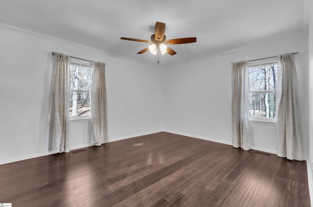 unfurnished room featuring dark wood-style flooring, a ceiling fan, baseboards, visible vents, and crown molding