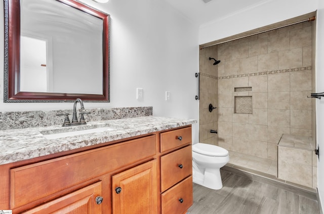 bathroom featuring a tile shower, vanity, and toilet