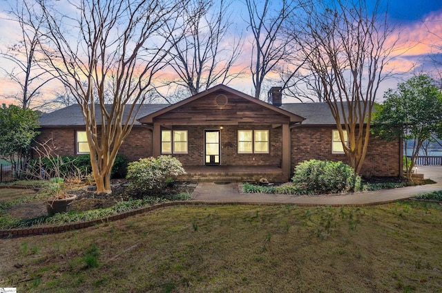 ranch-style house featuring a front yard, a chimney, a porch, and brick siding