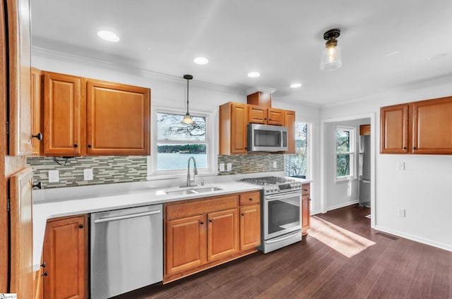 kitchen with ornamental molding, dark wood-style flooring, stainless steel appliances, light countertops, and a sink