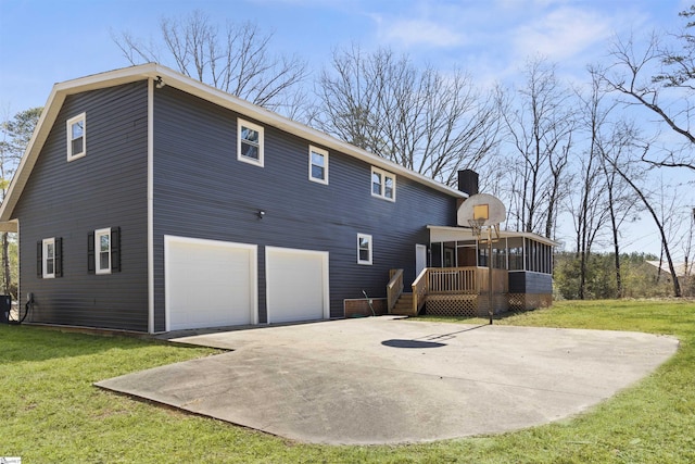 rear view of house featuring an attached garage, a lawn, a chimney, and a sunroom