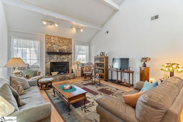 living area with visible vents, a stone fireplace, wood finished floors, high vaulted ceiling, and beamed ceiling